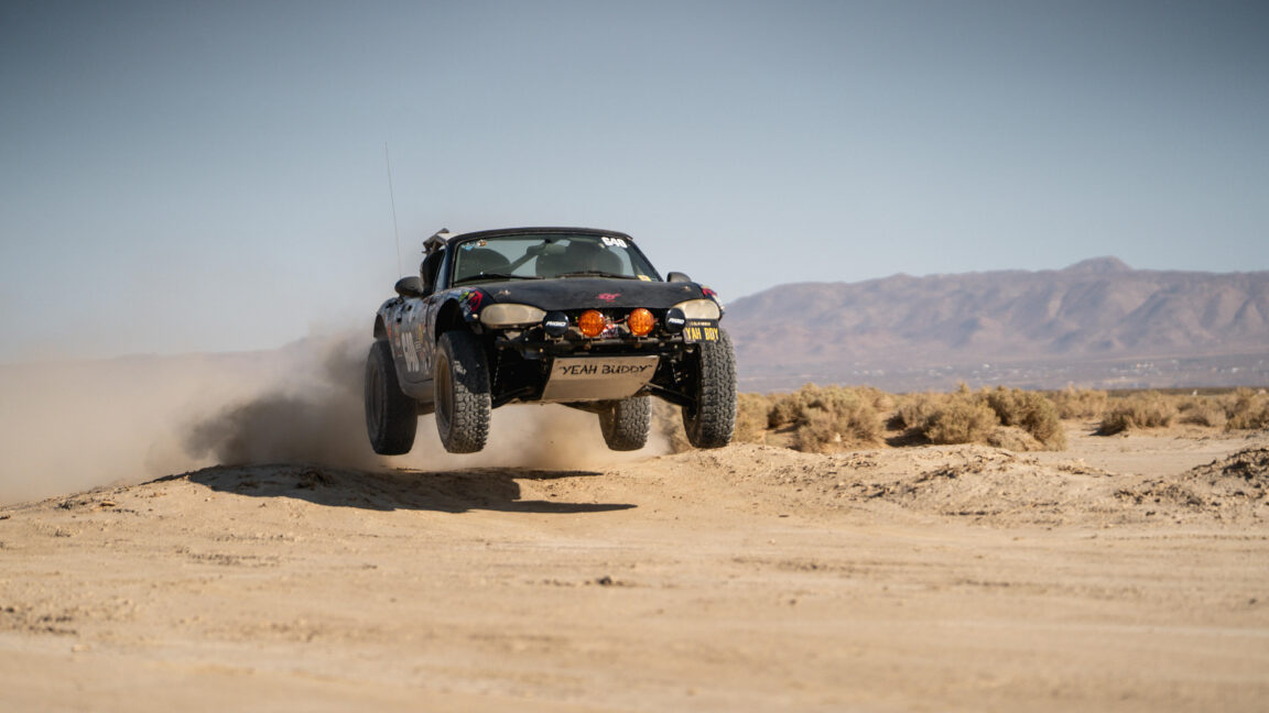 An off-road modified Miata gets some air as it drives off-road.